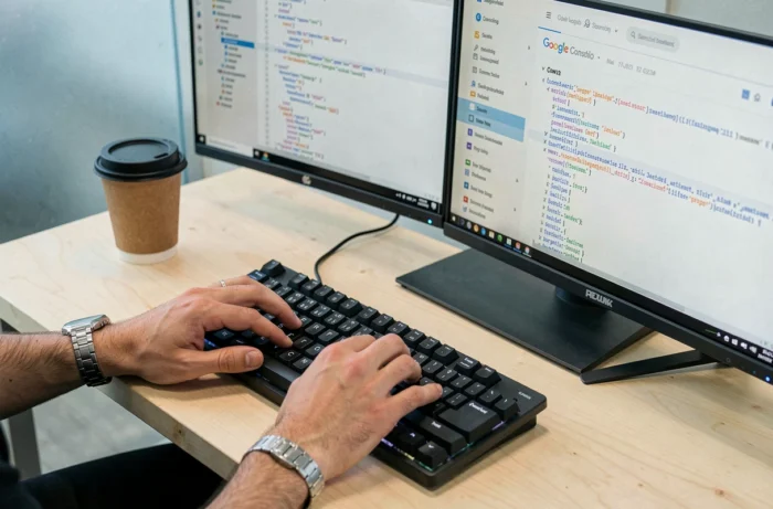 Mains d'un développeur tapant sur un clavier mécanique avec un sitemap XML et Google Search Console affichés sur deux moniteurs