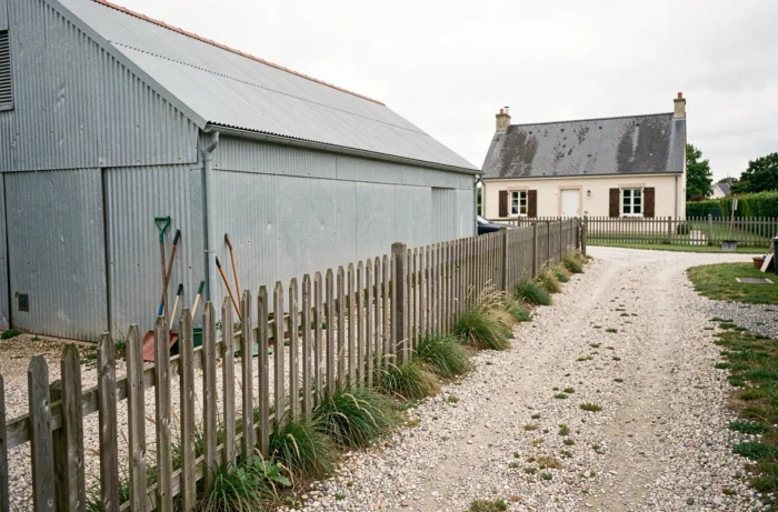 Hangar agricole en acier installé près d'une clôture en bois séparant deux propriétés résidentielles rurales